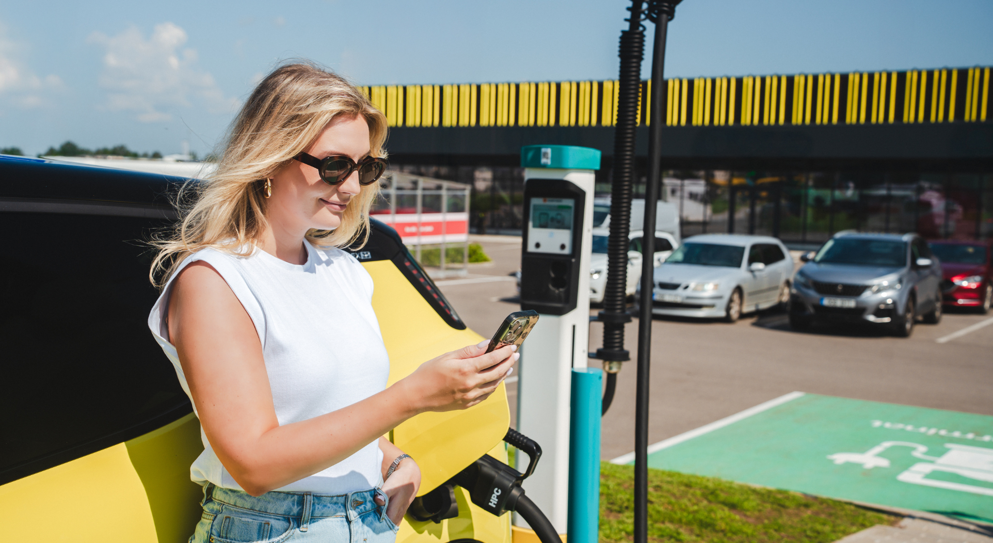 Tüdruk, kes kasutab mobiiltelefoni samal ajal kui auto on elektrilaadijas.
